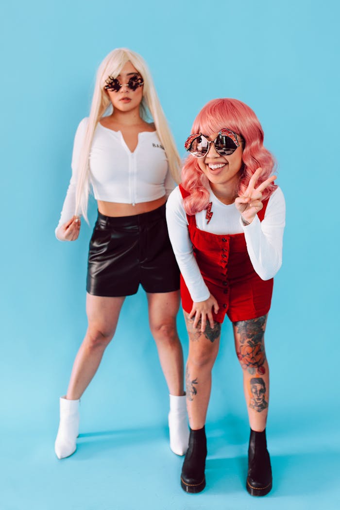 Two women in trendy wigs and sunglasses pose against a blue background.